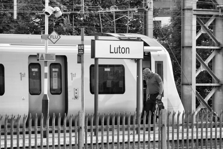 Image of multiple modern commuter trains on railway tracks near Ilford Station, with yellow and grey exterior finishes, set against an urban backdrop with buildings and trees. The tracks are clean and